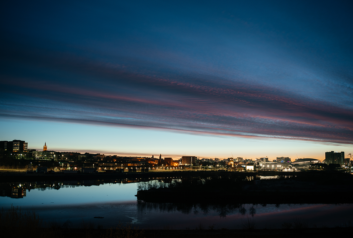 Blue hour view of Glasgow skyline with city lights reflecting on the River Clyde.
